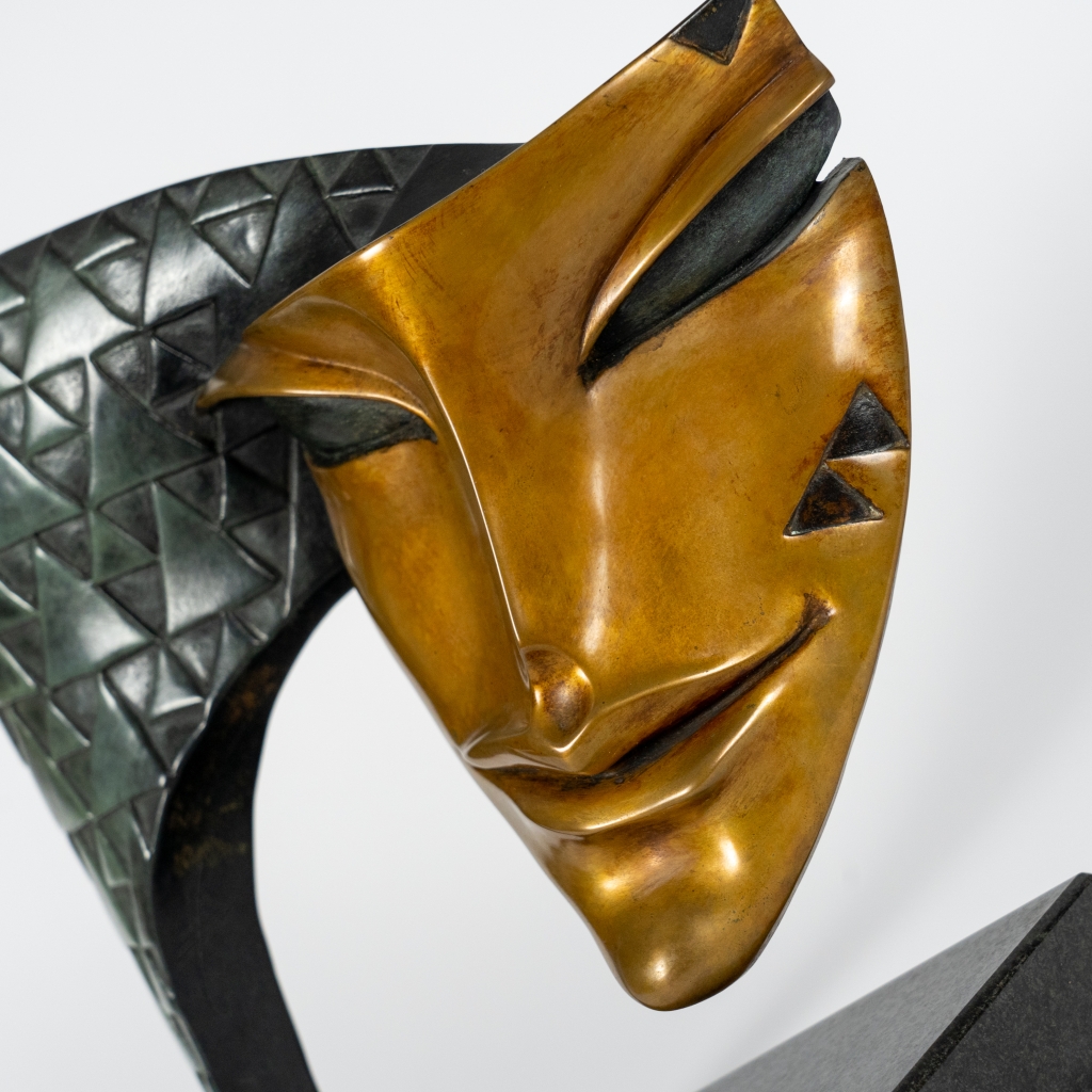 Zoom sur Arlequin d'Arsen Avetissian, sculpture contemporaine en bronze représentant un masque stylisé suspendu à une arche finement texturée de motifs géométriques. Son regard mi-clos et son sourire énigmatique évoquent le célèbre personnage de la Commedia dell'arte.
