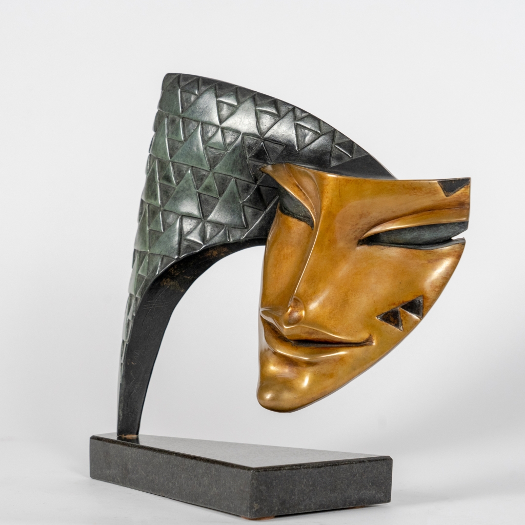 Vue de trois quarts d'Arlequin d'Arsen Avetissian, sculpture contemporaine en bronze représentant un masque stylisé suspendu à une arche finement texturée de motifs géométriques. Son regard mi-clos et son sourire énigmatique évoquent le célèbre personnage de la Commedia dell'arte.
