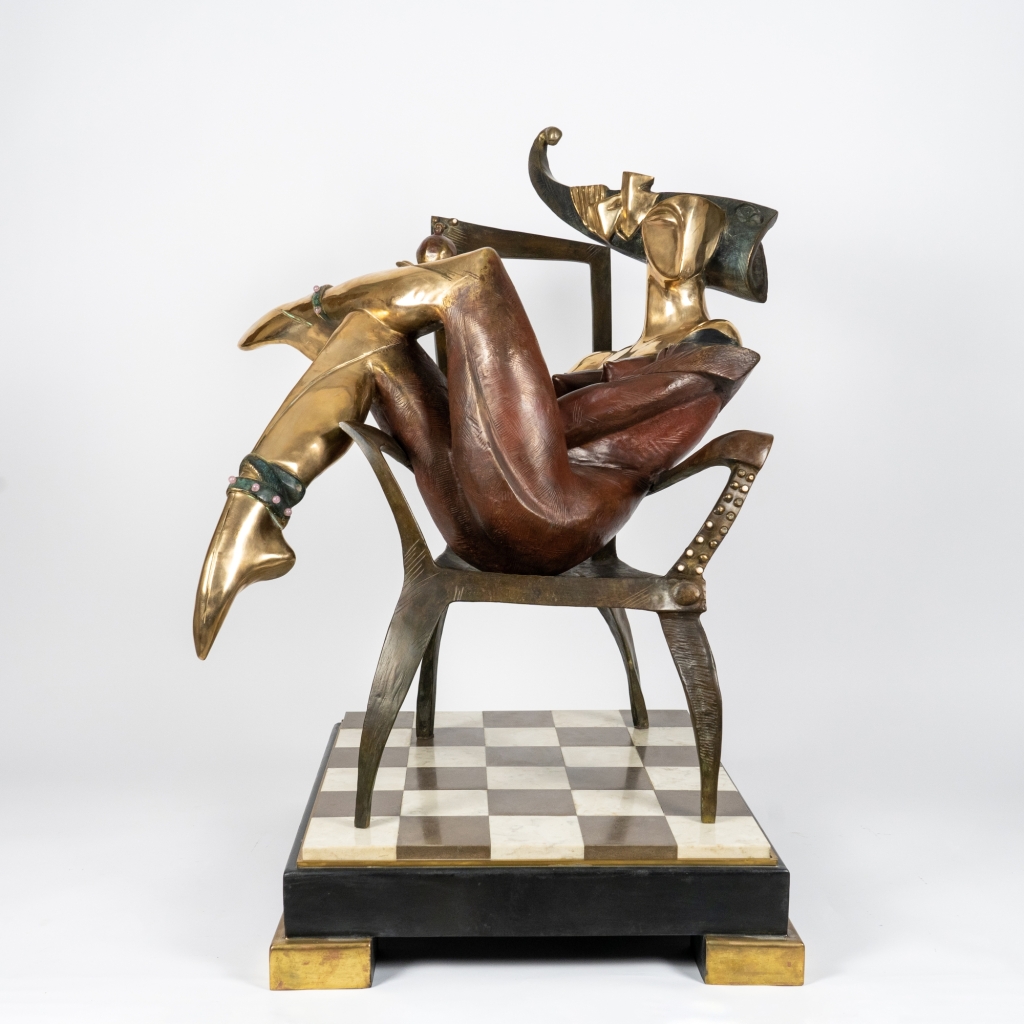 La Reine de trèfle d’Arsen Avetissian, sculpture en bronze représentant une figure féminine stylisée assise sur un fauteuil, jambes croisées, évoluant dans un univers inspiré du jeu de cartes. L’œuvre repose sur un damier noir et blanc qui renforce son caractère symbolique et théâtral.