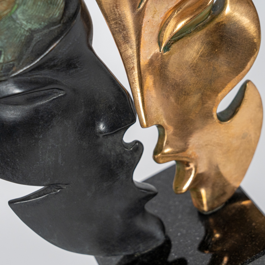 Detail des masques Mascarade d'Arsen Avetissian, sculpture contemporaine en bronze représentant deux figures stylisées se faisant face. Les silhouettes, intégrées à deux formes évoquant des masques, jouent sur les contrastes de patines noires, dorées et vertes dans une composition élégante et symbolique.
