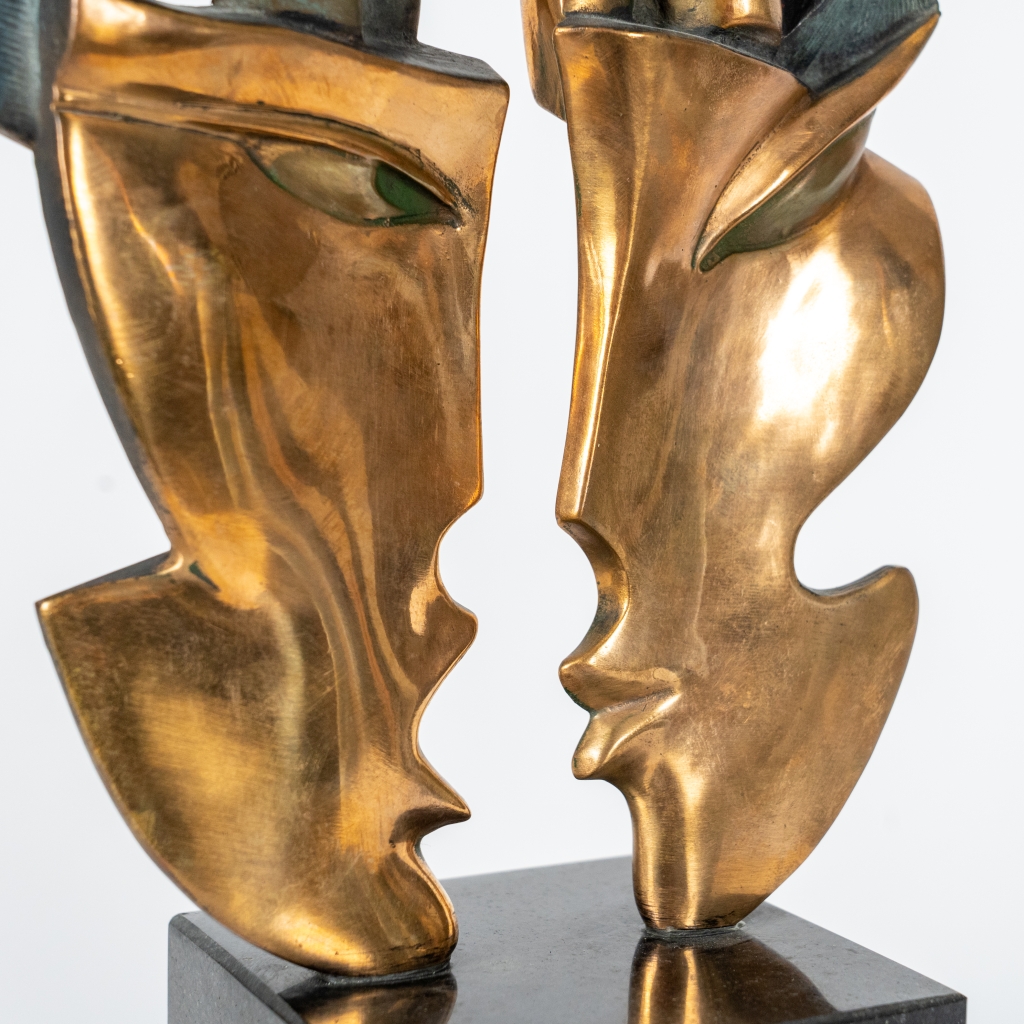 Zoom sur les masques de Mascarade III d'Arsen Avetissian, sculpture contemporaine en bronze représentant deux personnages stylisés dominant deux grands masques se faisant face. Les patines dorées, vertes et bleutées renforcent le caractère symbolique de cette composition élégante.