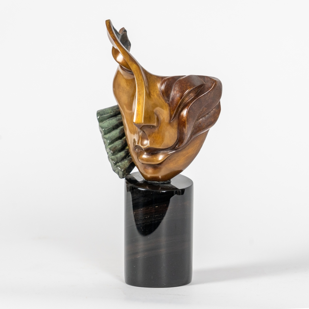 Vue de Nathalie d'Arsen Avetissian, sculpture contemporaine en bronze représentant un visage féminin stylisé aux lignes fluides et asymétriques. Les volumes polis et les nuances chaleureuses du bronze sont rehaussés d'un élément texturé vert-de-gris sur un socle cylindrique en pierre noire.