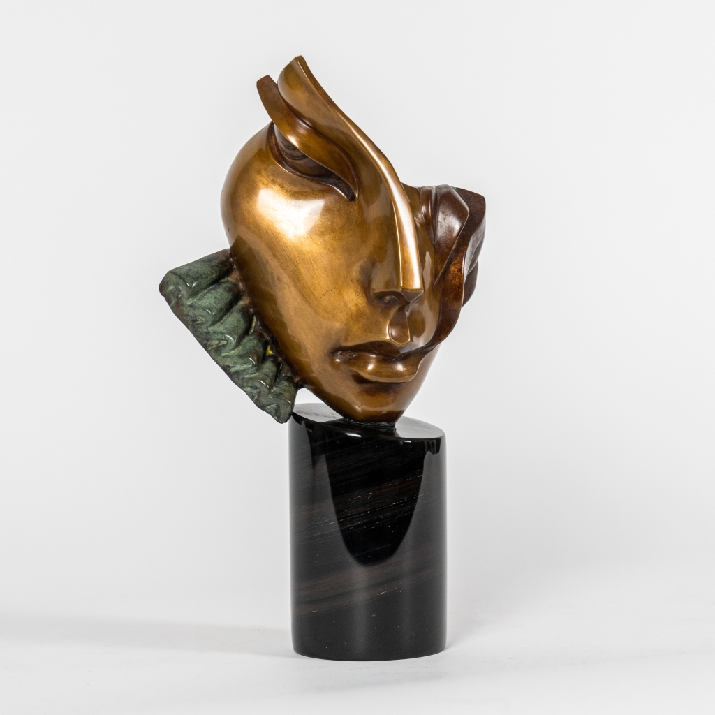Vue de trois quarts de Nathalie d'Arsen Avetissian, sculpture contemporaine en bronze représentant un visage féminin stylisé aux lignes fluides et asymétriques. Les volumes polis et les nuances chaleureuses du bronze sont rehaussés d'un élément texturé vert-de-gris sur un socle cylindrique en pierre noire.