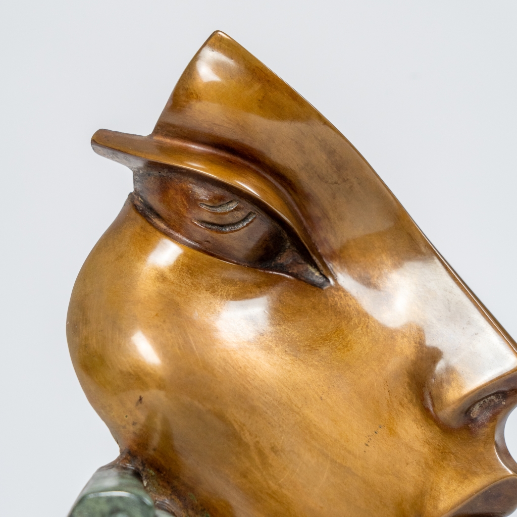 Zoom de Nathalie d'Arsen Avetissian, sculpture contemporaine en bronze représentant un visage féminin stylisé aux lignes fluides et asymétriques. Les volumes polis et les nuances chaleureuses du bronze sont rehaussés d'un élément texturé vert-de-gris sur un socle cylindrique en pierre noire.