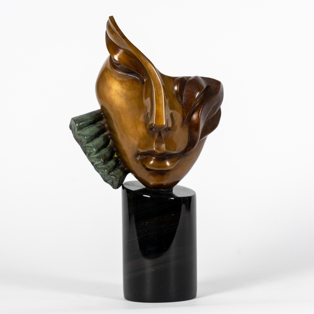 Nathalie d'Arsen Avetissian, sculpture contemporaine en bronze représentant un visage féminin stylisé aux lignes fluides et asymétriques. Les volumes polis et les nuances chaleureuses du bronze sont rehaussés d'un élément texturé vert-de-gris sur un socle cylindrique en pierre noire.