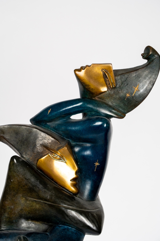 Plan sur les amoureux de Star à Venise d'Arsen Avetissian, sculpture contemporaine en bronze représentant un personnage élancé portant dans ses bras une figure masquée. Les silhouettes stylisées, aux patines bleues, dorées et vertes, reposent sur un socle circulaire en damier évoquant l'univers du carnaval vénitien.