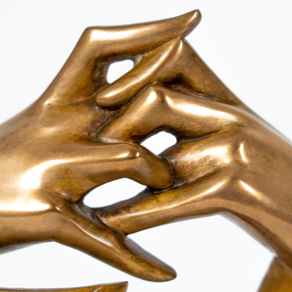 Zoom sur les mains de Un peu de soleil dans le froid d'Arsen Avetissian, sculpture contemporaine en bronze représentant un visage féminin stylisé encadré par deux bras levés dont les mains se rejoignent avec grâce. Les lignes fluides et la patine dorée créent une composition élégante, montée sur un socle en pierre.