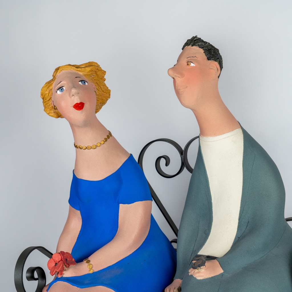 Zoom sur le couple amoureux 10 d’Evelyne Almayrac, sculpture unique en grès réfractaire représentant un couple assis sur un banc en fer forgé dans une scène pleine de tendresse.