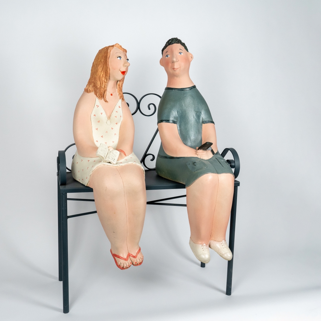 Vue de biais du couple amoureux 4 d’Evelyne Almayrac, sculpture unique en grès réfractaire représentant un couple assis sur un banc en fer forgé dans un moment de complicité.